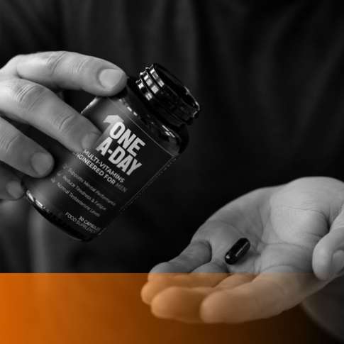 Person taking a One A-Day multivitamin capsule from the bottle