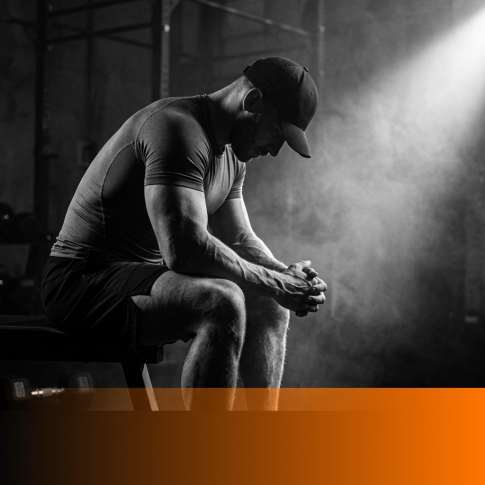 MenTools feature image for how to stay motivated as a man, cinematic black and white photograph of a fit man gathering himself in a dark gym under a dramatic light beam through haze, orange fade