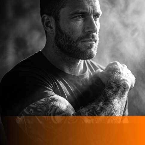 MenTools feature image for confidence vs arrogance for men, tight black and white portrait of a composed self-assured man in dramatic side light with orange fade