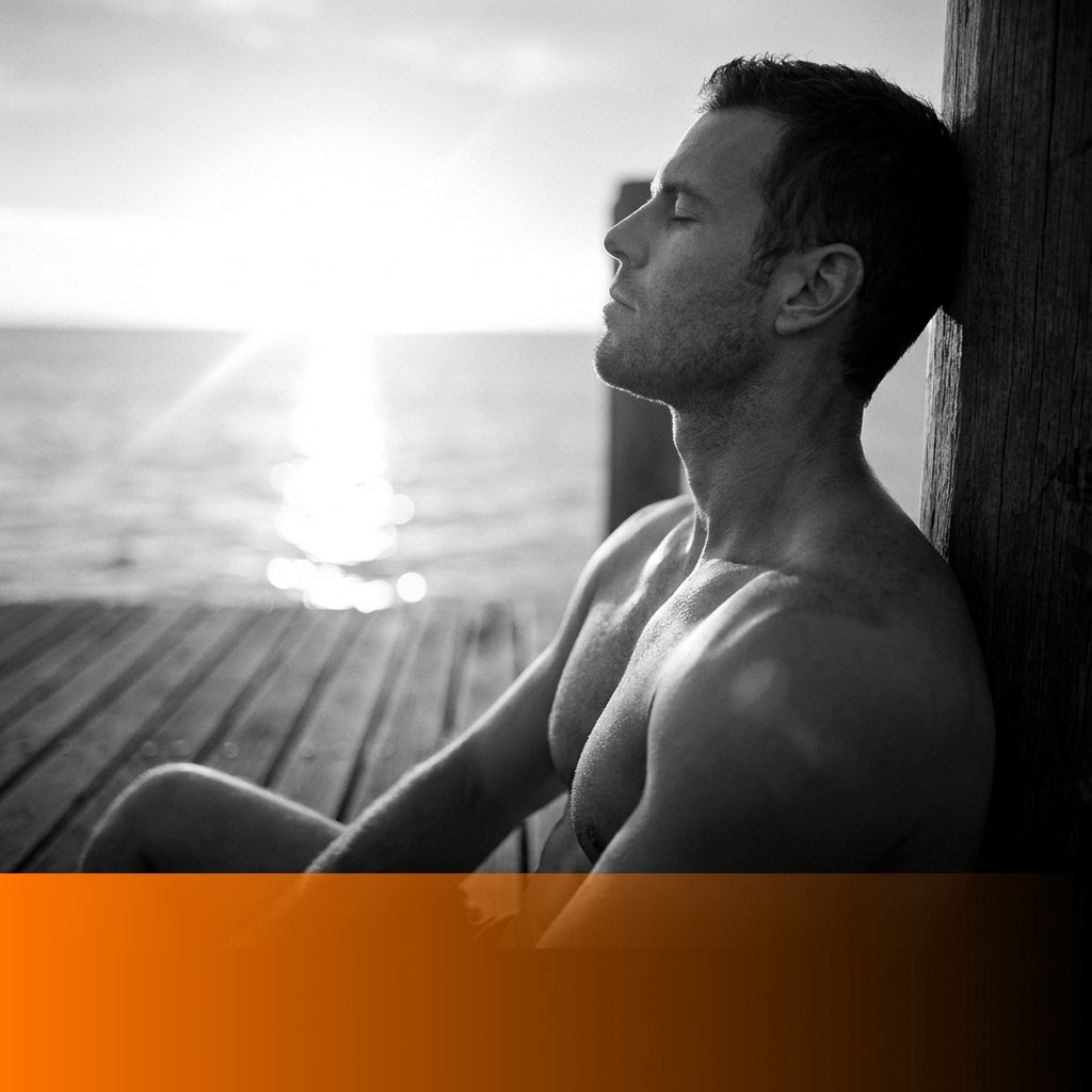 MenTools blog feature image for does breathwork lower stress, black and white photograph of a man sitting on a timber jetty at sunrise with light on the water, orange MenTools overlay band