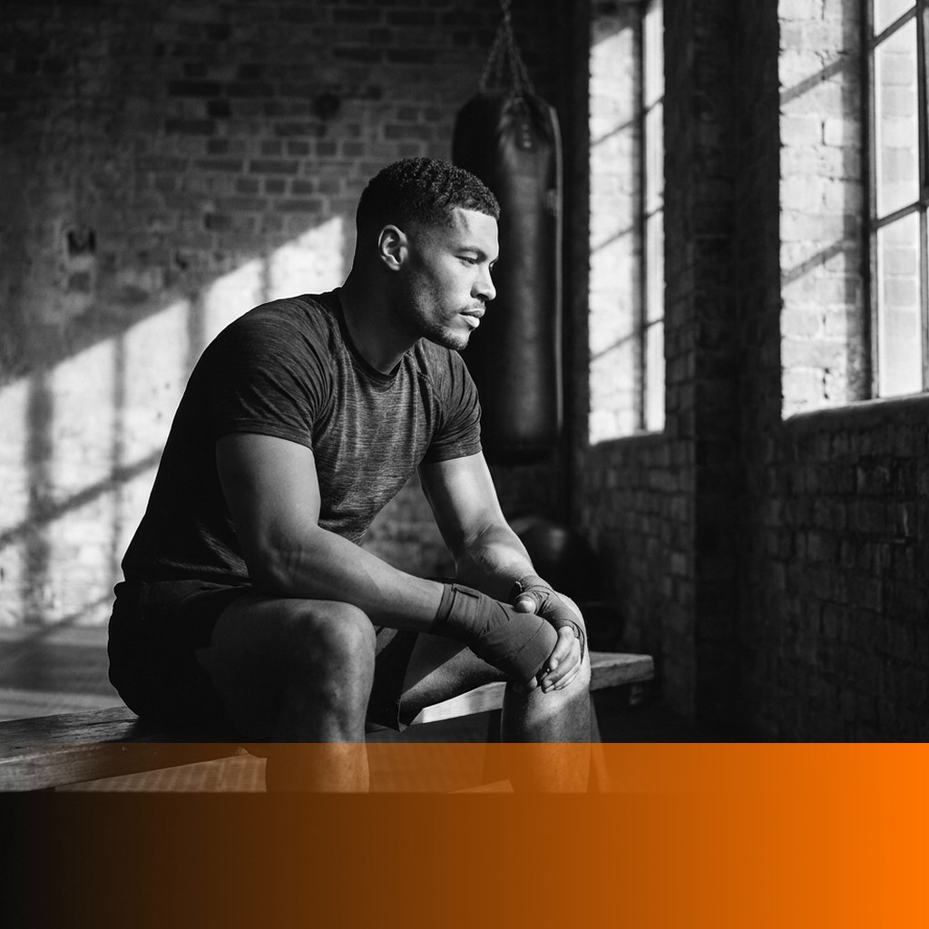 MenTools feature image, a man in hand wraps sits on a bench in a brick boxing gym between rounds, composed and focused, for a post on what mental fitness is and how men train it